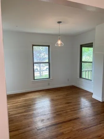 an empty room with wooden floor chandelier and windows
