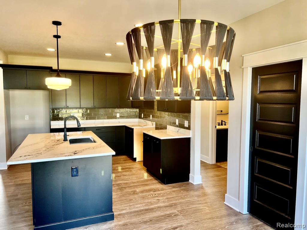 5382 Spring Meadows Way Linden, MI 48451 - Photo 7 of 20 Kitchen with light stone counters, a center island with sink, light wood-type flooring, hanging light fixtures, and backsplash