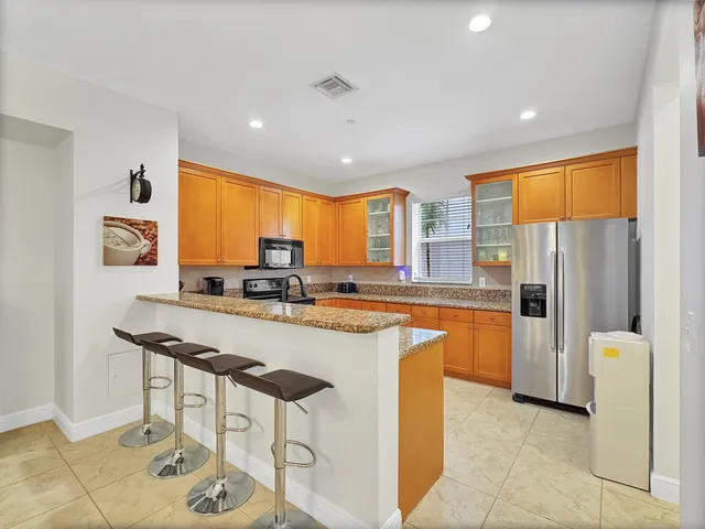 a kitchen with stainless steel appliances granite countertop a refrigerator a sink dishwasher a stove and a dining table with wooden cabinet