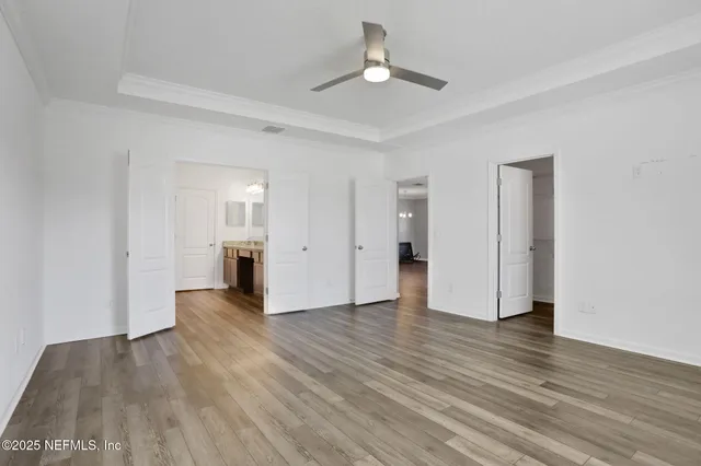 a view of an empty room with wooden floor and a ceiling fan