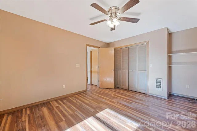 a view of an empty room with wooden floor and a ceiling fan