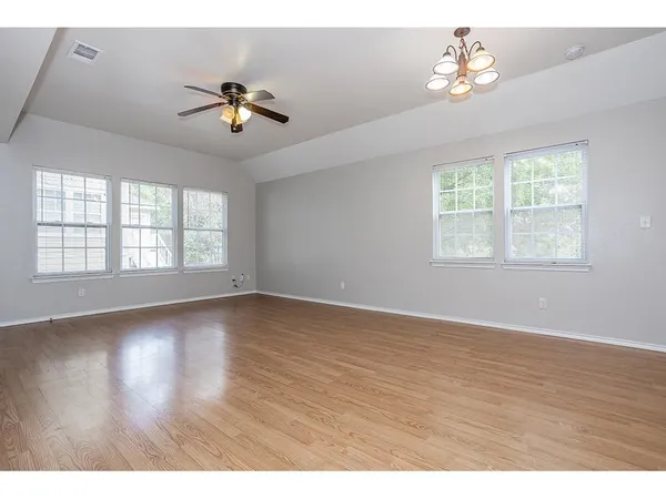 an empty room with wooden floor chandelier fan and windows