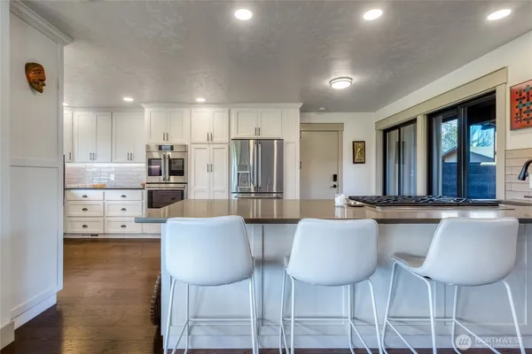 a kitchen with stainless steel appliances kitchen island granite countertop a dining table chairs and a refrigerator