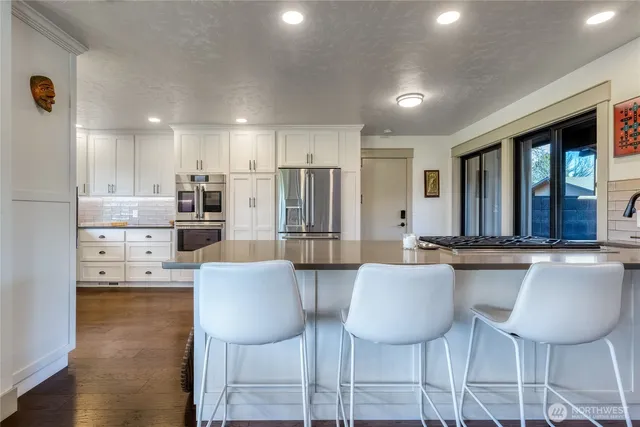 a kitchen with stainless steel appliances kitchen island granite countertop a dining table chairs and a refrigerator