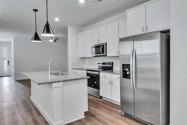 a kitchen with kitchen island granite countertop a refrigerator a sink a stove and white cabinets