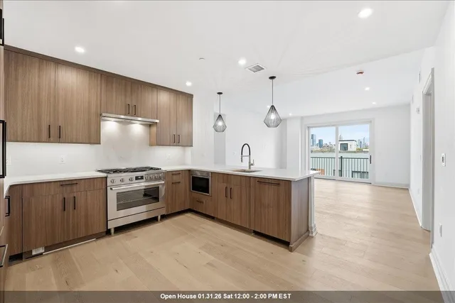 a large kitchen with stainless steel appliances wooden cabinets a stove a sink and a large window