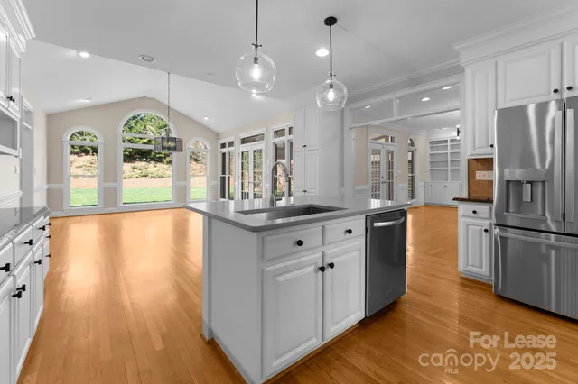 a kitchen with stainless steel appliances granite countertop a refrigerator a sink dishwasher a oven and a dining table with wooden floor