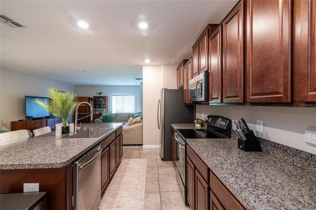 5127 Sable Chime Drive Wimauma, FL 33598 - Photo 11 of 56 a kitchen with granite countertop stainless steel appliances a sink dishwasher stove refrigerator and cabinets