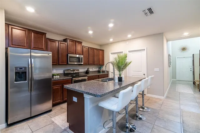 a kitchen with stainless steel appliances granite countertop a refrigerator a sink a stove a dining table and chairs