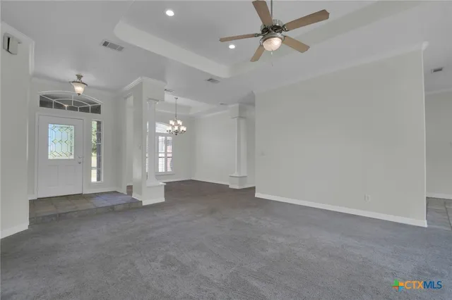 an empty room with chandelier fan and windows
