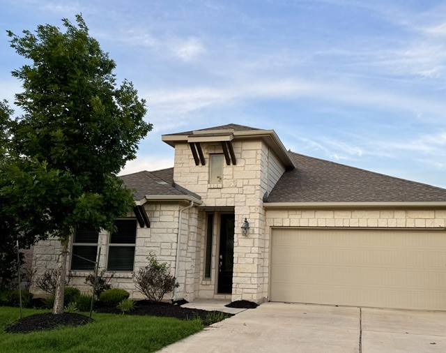 Contemporary stone veneer facade featuring a prominent entryway with a vertical window, dark roof shingles, and an attached two-car garage