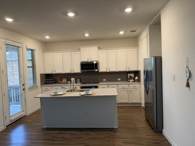 2016 Wooded Run Trail Georgetown, TX 78628 - Photo 5 of 16 Kitchen featuring white shaker cabinetry, stainless steel appliances, a center island with sink, wood-finish flooring, and a glass-paneled door to an exterior space