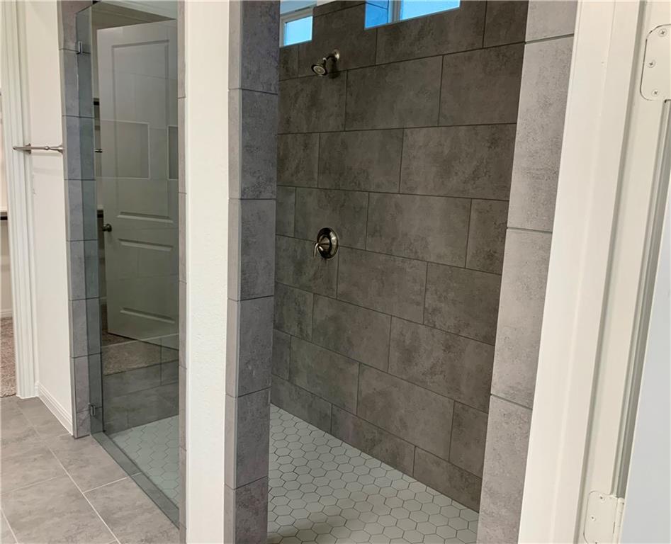 2016 Wooded Run Trail Georgetown, TX 78628 - Photo 10 of 16 Modern walk-in shower featuring glass panel enclosure, large format grey wall tiles, a hexagonal tile floor, and chrome fixtures