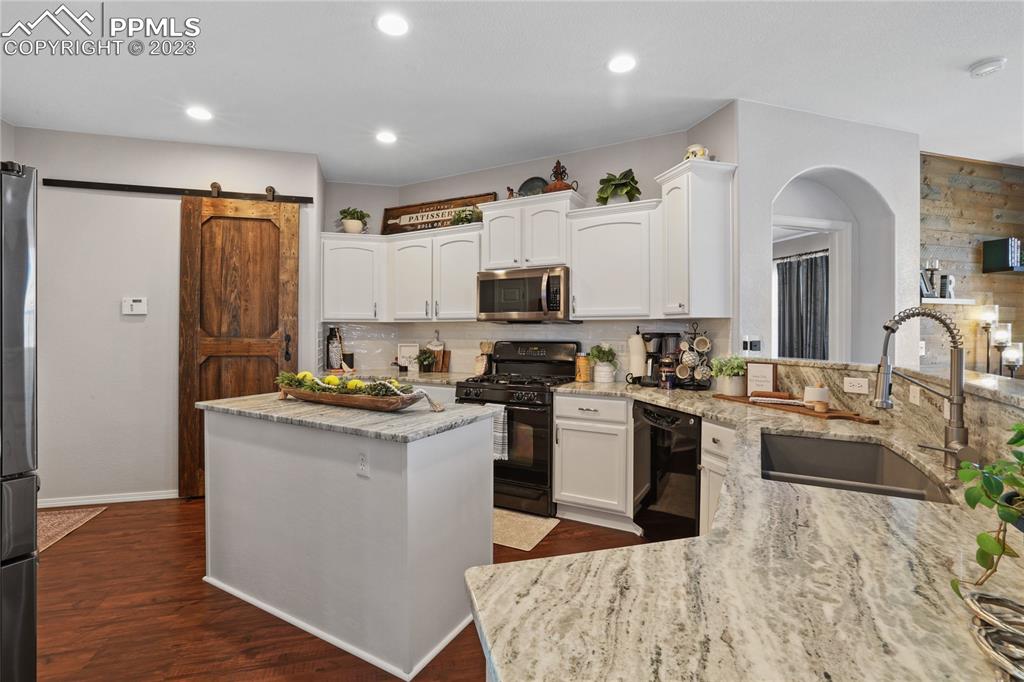 6435 Coyote Ridge Court Colorado Springs, CO 80923 - Photo 17 of 50 a kitchen with stainless steel appliances granite countertop a stove top oven a sink dishwasher a refrigerator and a dining table with wooden floor