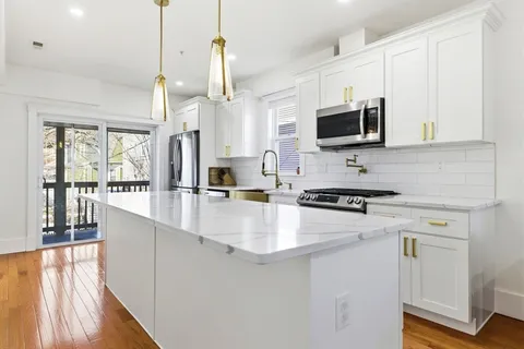 a kitchen with stainless steel appliances a stove a sink a microwave a refrigerator a stove and white cabinets with wooden floor