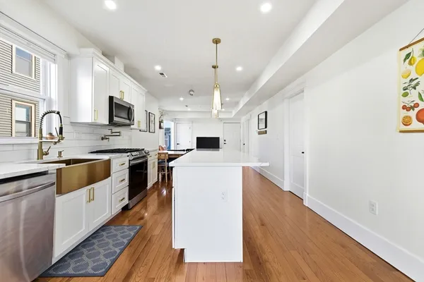 a large kitchen with stainless steel appliances granite countertop a white stove top oven a sink dishwasher and a refrigerator with wooden floor