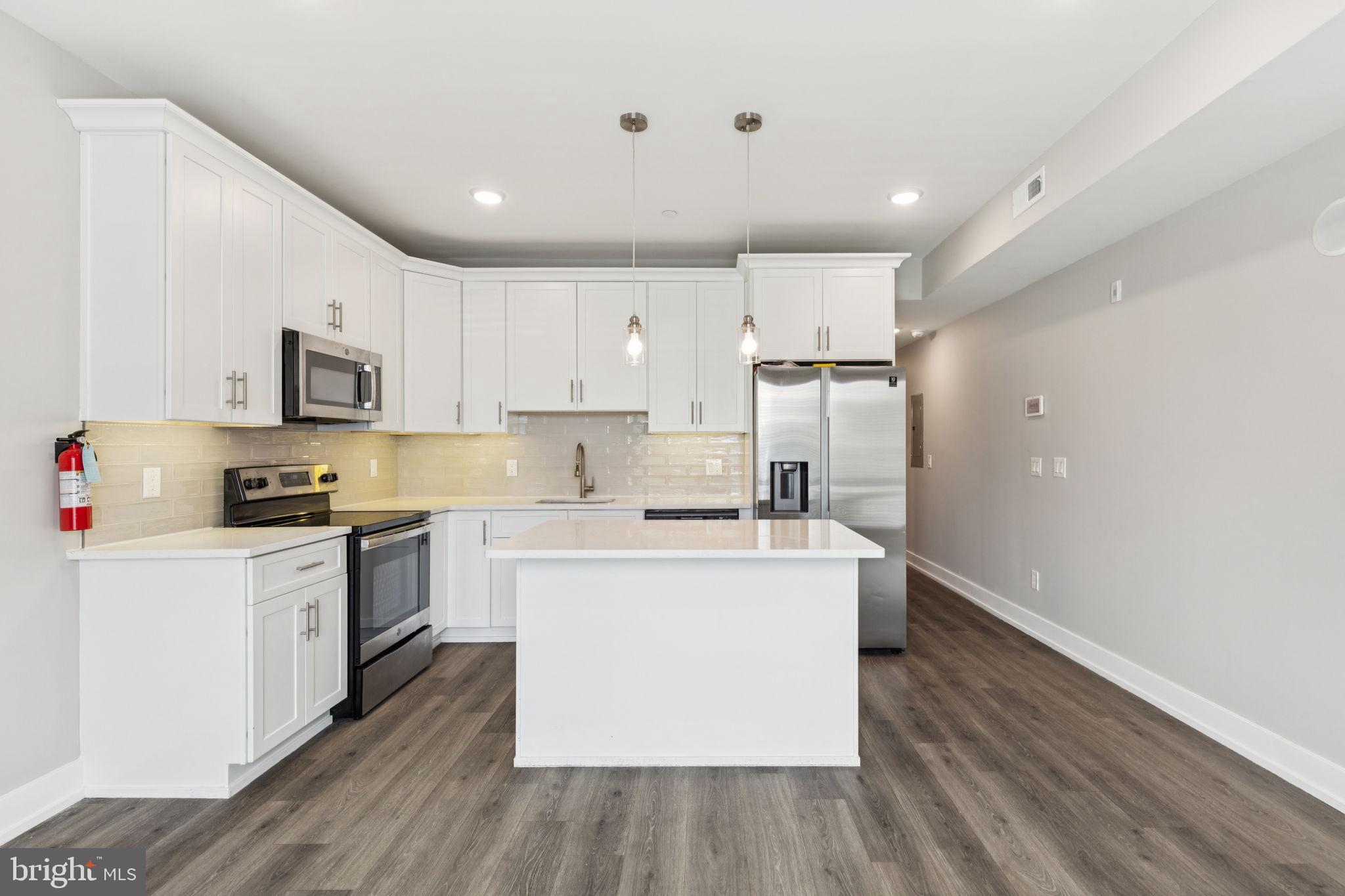 a kitchen with stainless steel appliances granite countertop a stove top oven a refrigerator a sink and dishwasher with wooden floor