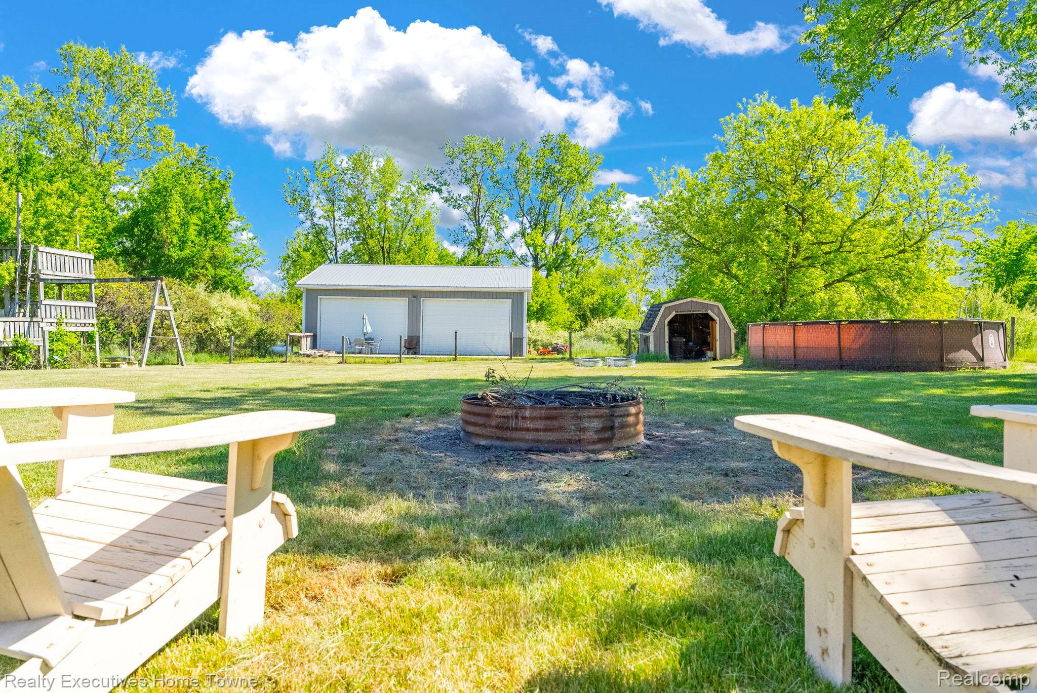 6560 Roach Road Lexington, MI 48450 - Photo 30 of 36 Expansive backyard featuring a central fire pit, substantial outbuilding with two garage doors, an additional barn structure, and an above-ground pool