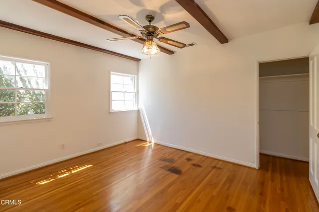 an empty room with wooden floor fan and windows