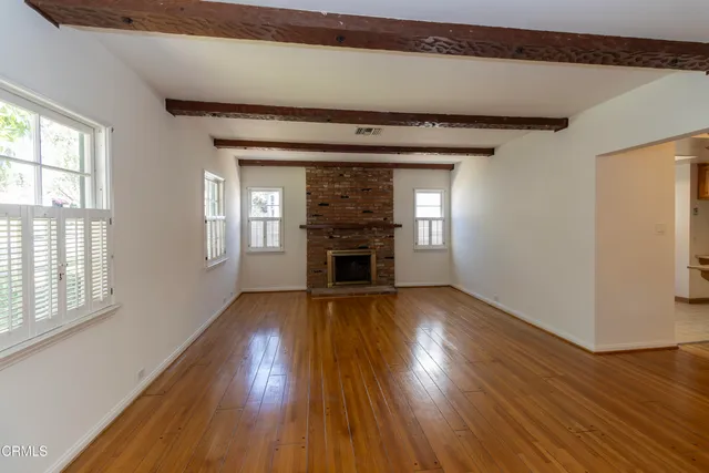 an empty room with wooden floor fireplace and windows
