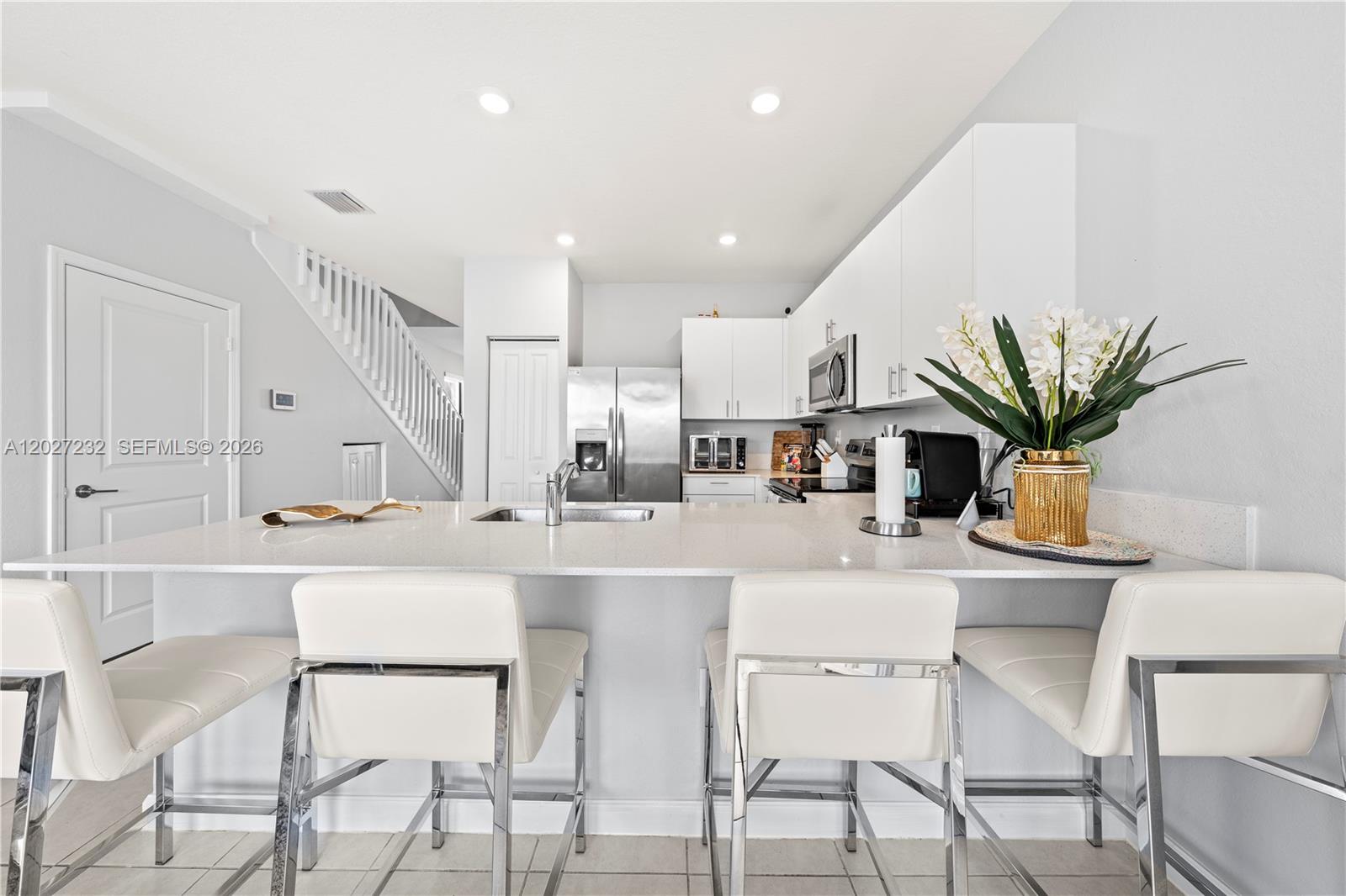 23489 Southwest 127th Place Homestead, FL 33032 - Photo 9 of 24 a white kitchen with stainless steel appliances kitchen island granite countertop a dining table chairs and white cabinets