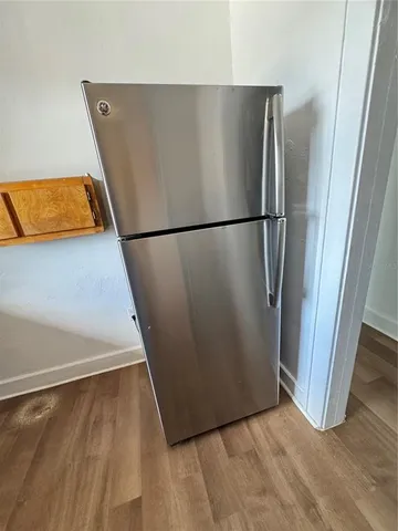 a view of a refrigerator in kitchen and an empty room with wooden floor