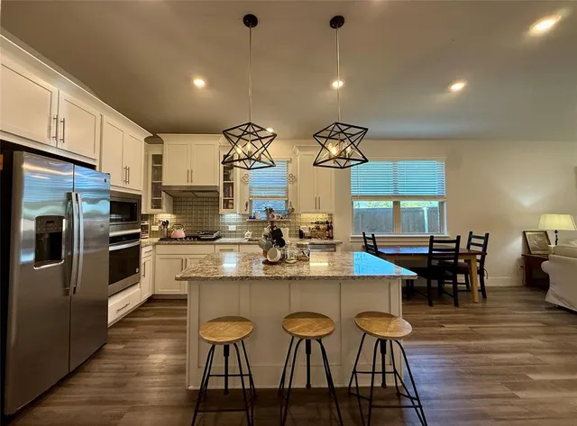 a kitchen with stainless steel appliances kitchen island granite countertop a table chairs and a refrigerator