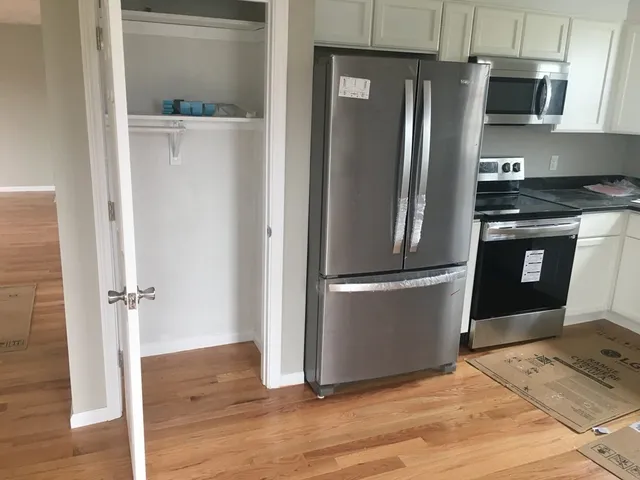a view of a refrigerator in kitchen and an empty room with wooden floor