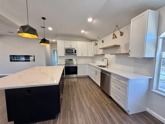 a kitchen with stainless steel appliances a sink a stove a refrigerator cabinets and wooden floor