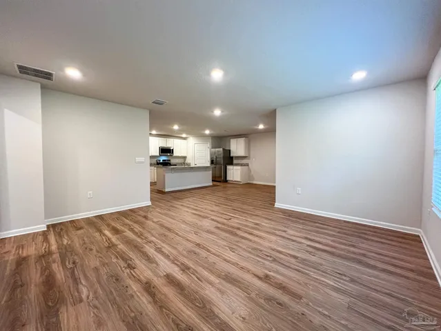 an empty room with wooden floor kitchen view and a kitchen