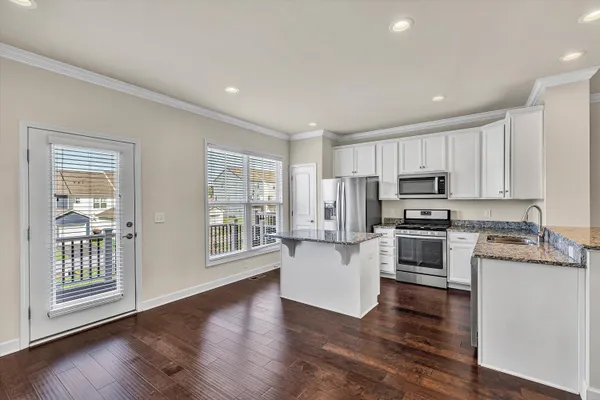 a large kitchen with stainless steel appliances granite countertop a stove top oven a refrigerator a sink and dishwasher with wooden floor