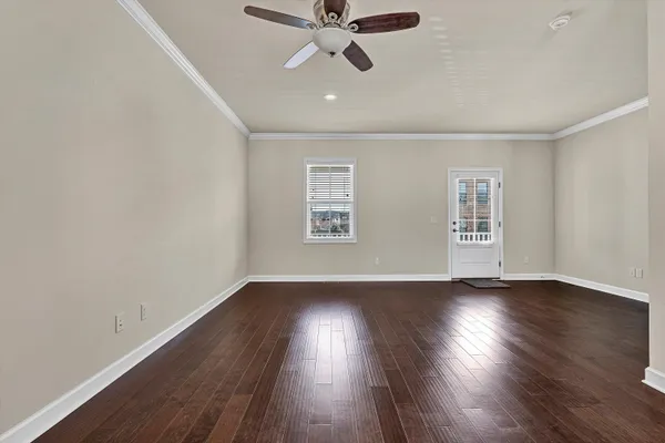 a view of an empty room with wooden floor and a ceiling fan