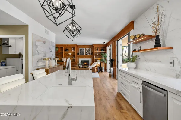 a view of a kitchen with kitchen island stainless steel appliances a stove a sink a chimney wooden floor and a view of living room