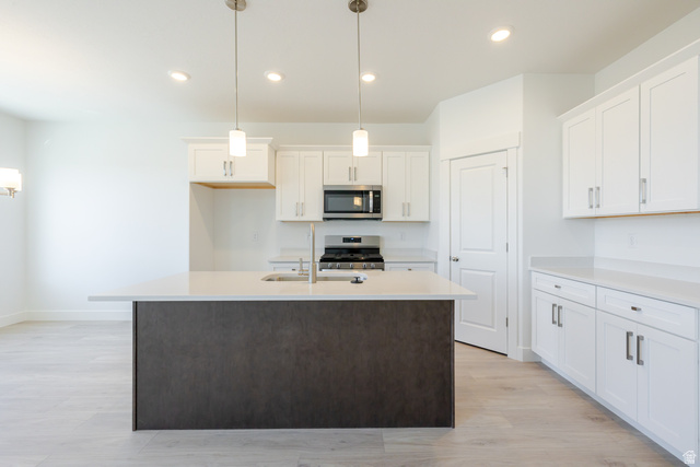 4720 Heartwood Road, Unit 438 Mapleton, UT 84664 - Photo 10 of 19 Kitchen with a center island with sink, light wood finished floors, stainless steel appliances, two tone cabinetry, and decorative light fixtures