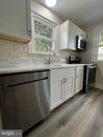 a kitchen with stainless steel appliances granite countertop a sink a stove a microwave a window and white cabinets