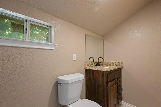a bathroom with a granite countertop toilet a sink and a window