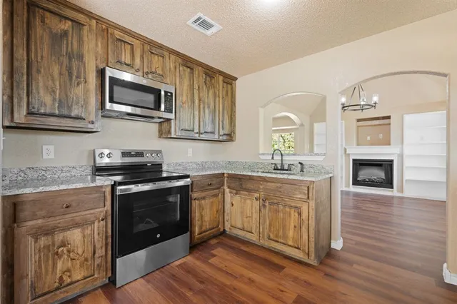 a kitchen with stainless steel appliances granite countertop a stove top oven a sink dishwasher and microwave with wooden floor