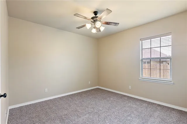 an empty room with chandelier fan and windows