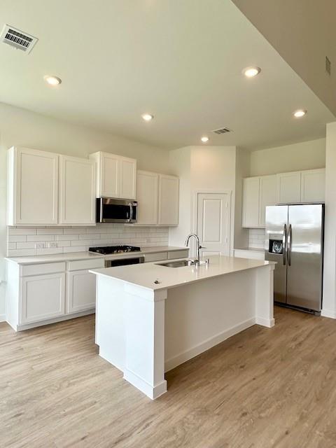 2204 Greenbelt Road Celina, TX 75009 - Photo 2 of 9 Modern kitchen featuring a central island with a sink, white cabinetry, light-toned countertops, a subway tile backsplash, and wood-finish flooring