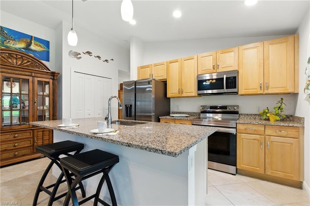 176 Venus Cay Naples, FL 34114 - Photo 17 of 50 Kitchen with appliances with stainless steel finishes, a kitchen bar, light stone counters, an island with sink, and light tile patterned flooring