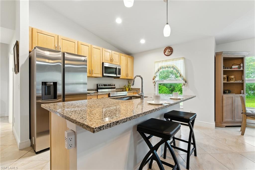 176 Venus Cay Naples, FL 34114 - Photo 18 of 50 Kitchen featuring stainless steel appliances, light brown cabinets, light stone counters, lofted ceiling, and pendant lighting