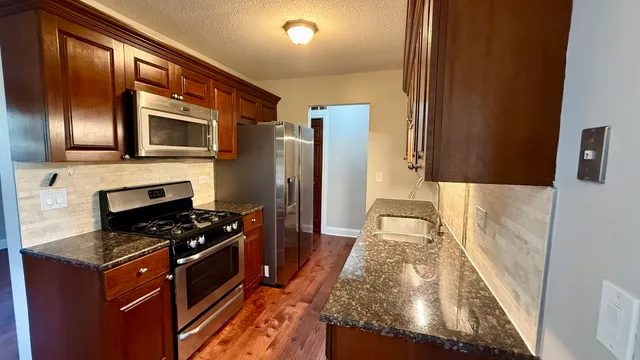 a kitchen with granite countertop stove top oven microwave and refrigerator