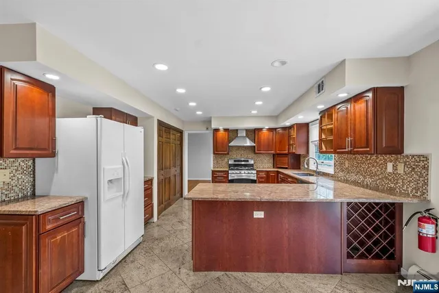 a kitchen with stainless steel appliances granite countertop a refrigerator a stove and a sink with wooden cabinets