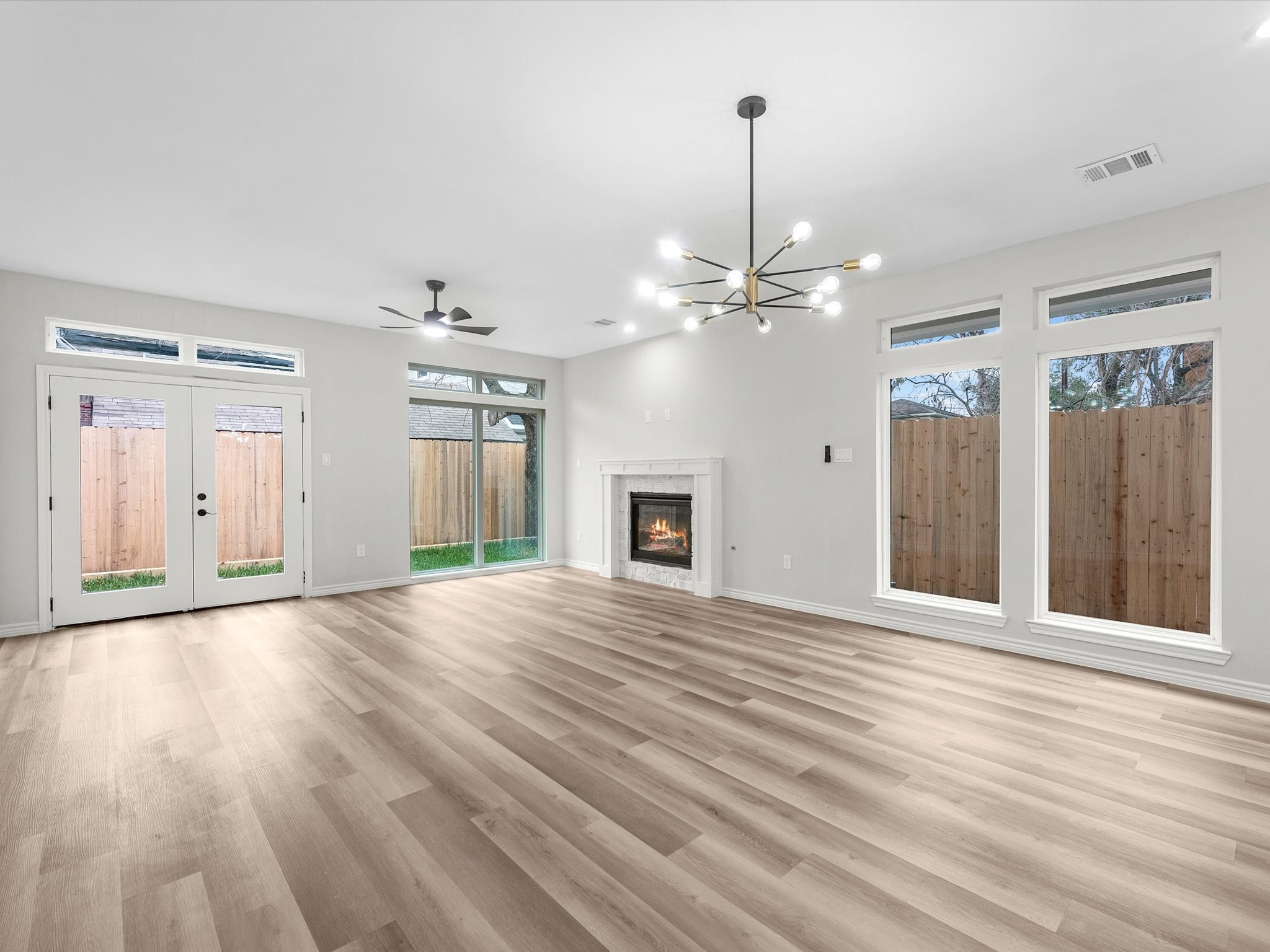 1319 West Bell Street Houston, TX 77019 - Photo 16 of 50 This spacious living room features large windows for natural light, a modern chandelier, ceiling fan, and a cozy fireplace. The light vinyl flooring and neutral walls create a warm, inviting atmosphere.
