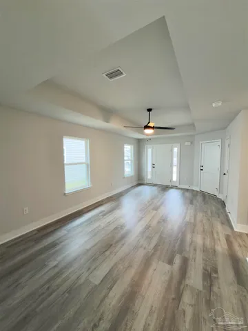 an empty room with wooden floor chandelier fan and windows