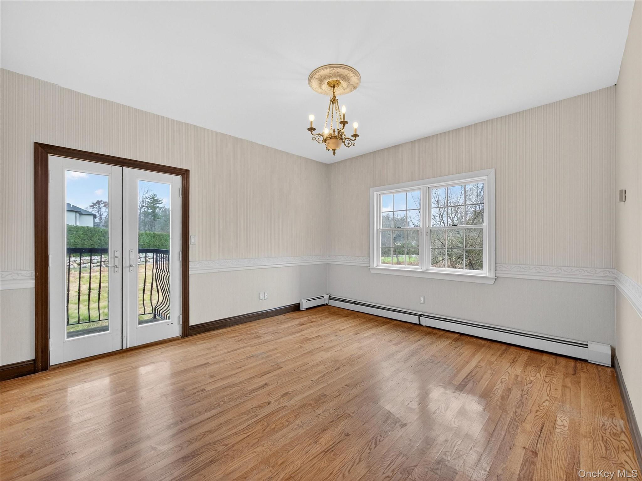 120 East Willow Tree Road Spring Valley, NY 10977 - Photo 15 of 49 Empty room featuring wallpapered walls, light wood-type flooring, baseboard heating, french doors, and a chandelier