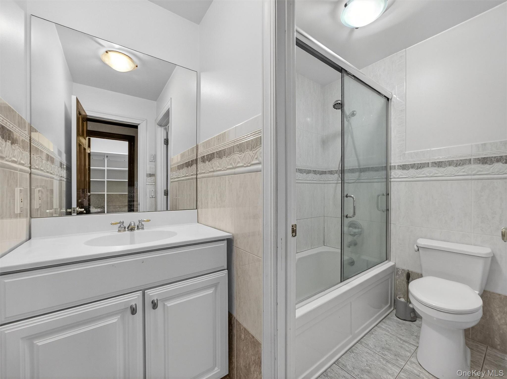 120 East Willow Tree Road Spring Valley, NY 10977 - Photo 19 of 49 Full bathroom with tile walls, vanity, bath / shower combo with glass door, wainscoting, and light tile patterned flooring