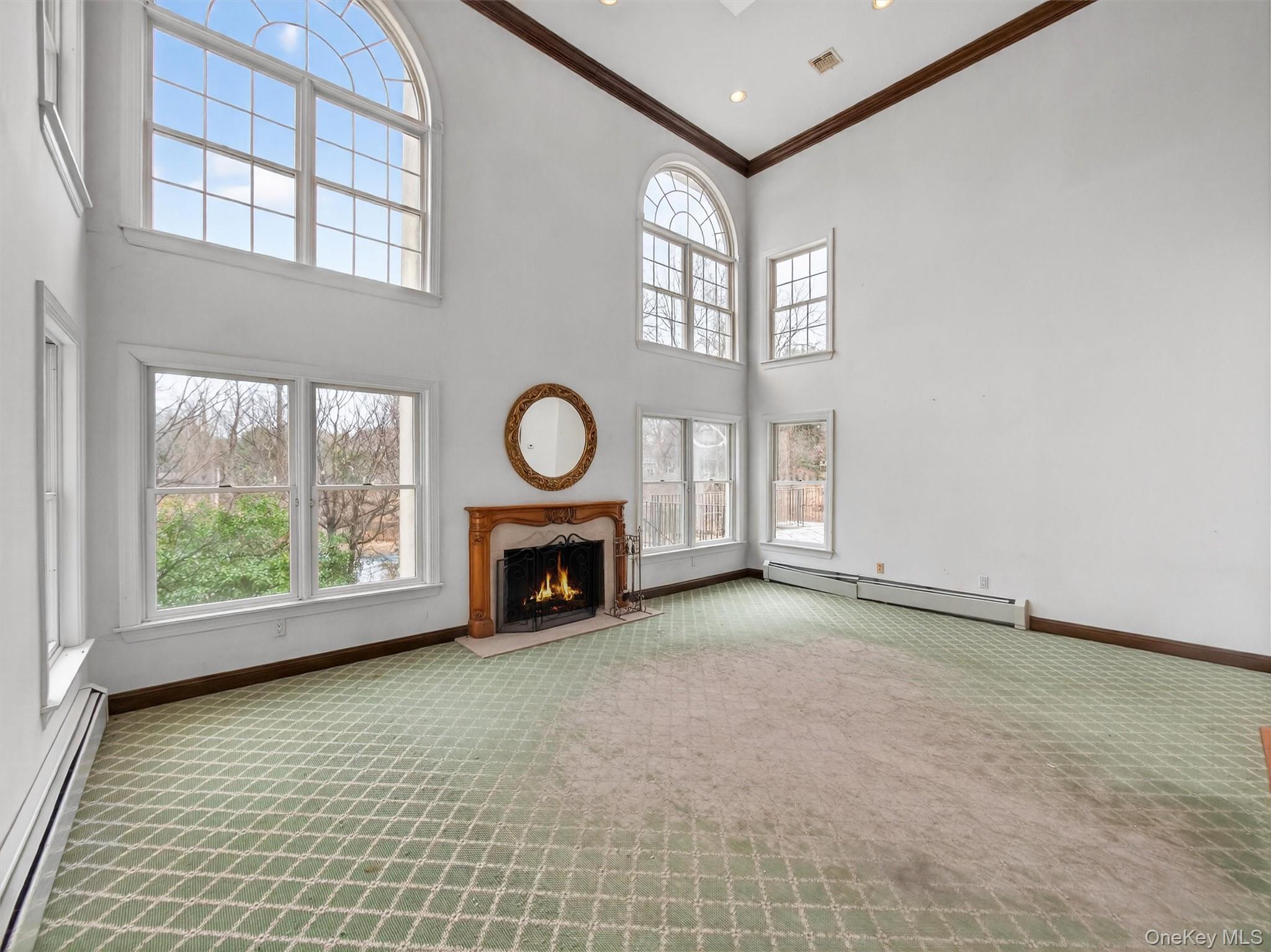 120 East Willow Tree Road Spring Valley, NY 10977 - Photo 9 of 49 Unfurnished living room with baseboard heating, a warm lit fireplace, light carpet, a high ceiling, and crown molding
