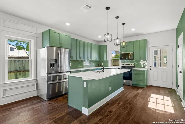 a kitchen with kitchen island granite countertop a refrigerator a sink dishwasher a kitchen island with wooden floor and cabinets