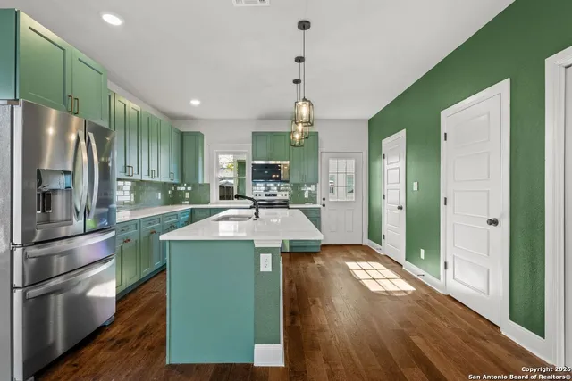 a kitchen with kitchen island granite countertop a refrigerator a sink dishwasher a stove and a dining table with wooden floor